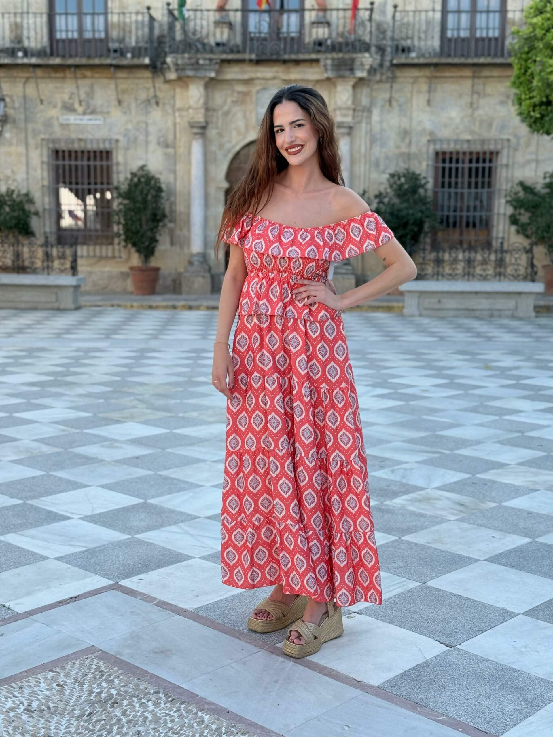 Mujer posando con vestido largo rojo coral con estampado geométrico y cuñas