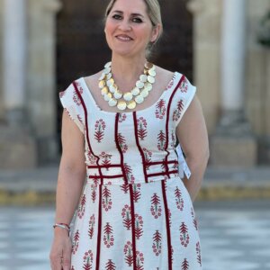 Medio plano de mujer luciendo vestido largo blanco con estampado floral burdeos y líneas geométricas, fondo arquitectónico