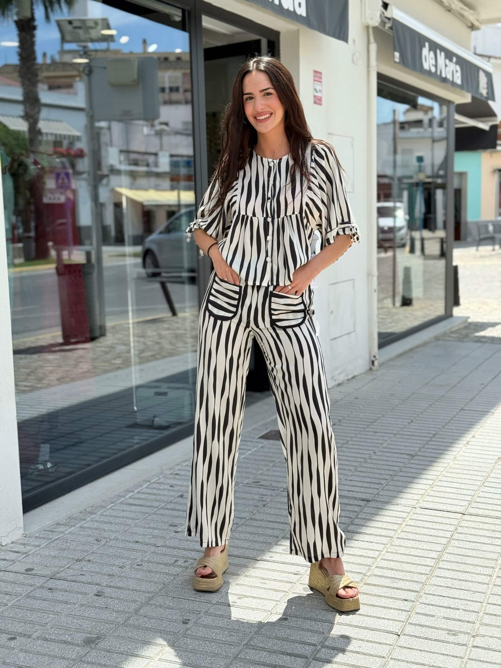 Mujer con conjunto blanco y negro de líneas verticales, blusa con bolsillos y pantalón recto, vista de cuerpo entero